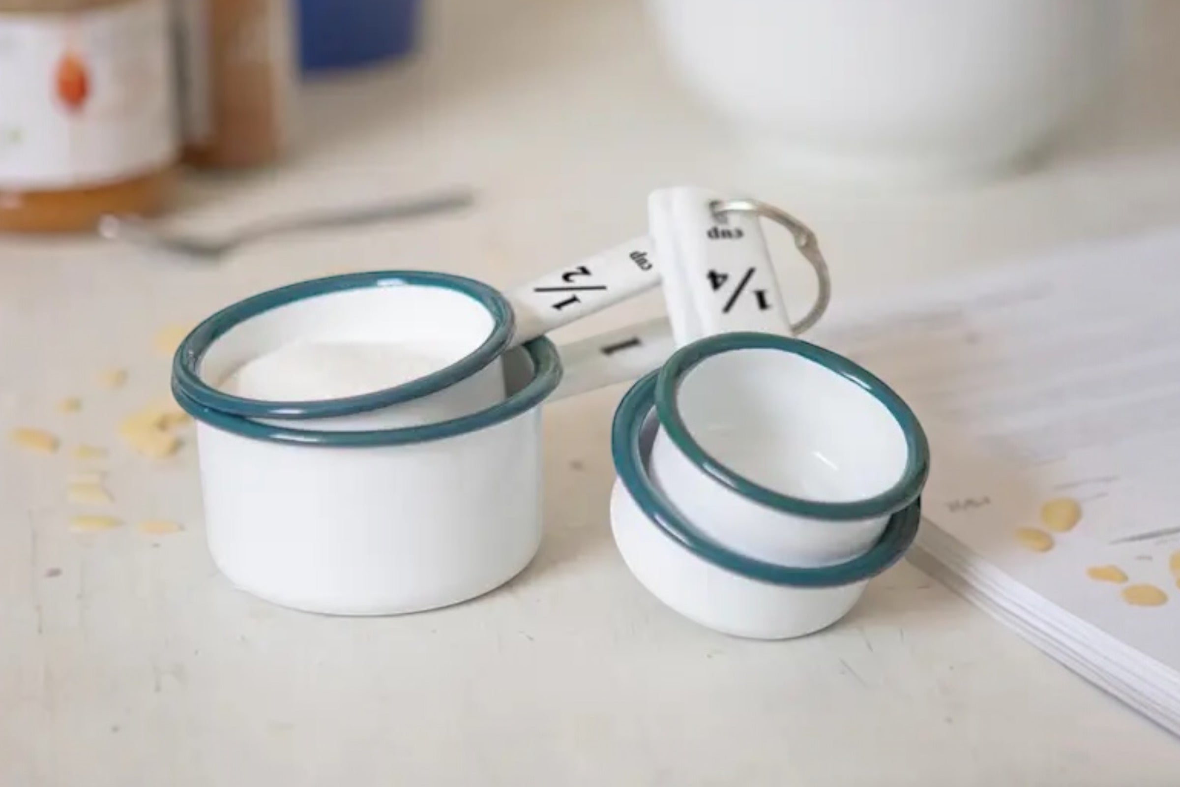 A set of four enamelled steel measuring cups finished in white with green accents. Set against a kitchen worktop.