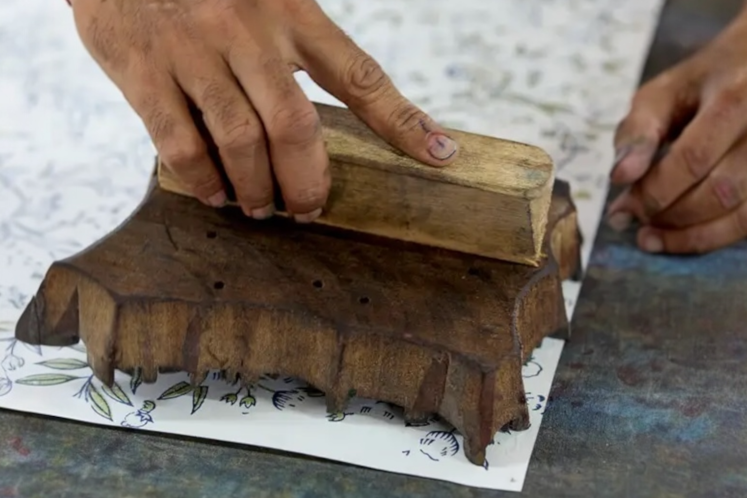 A craftsman's hands are captured block printing some handmade, song birds design wrapping paper.
