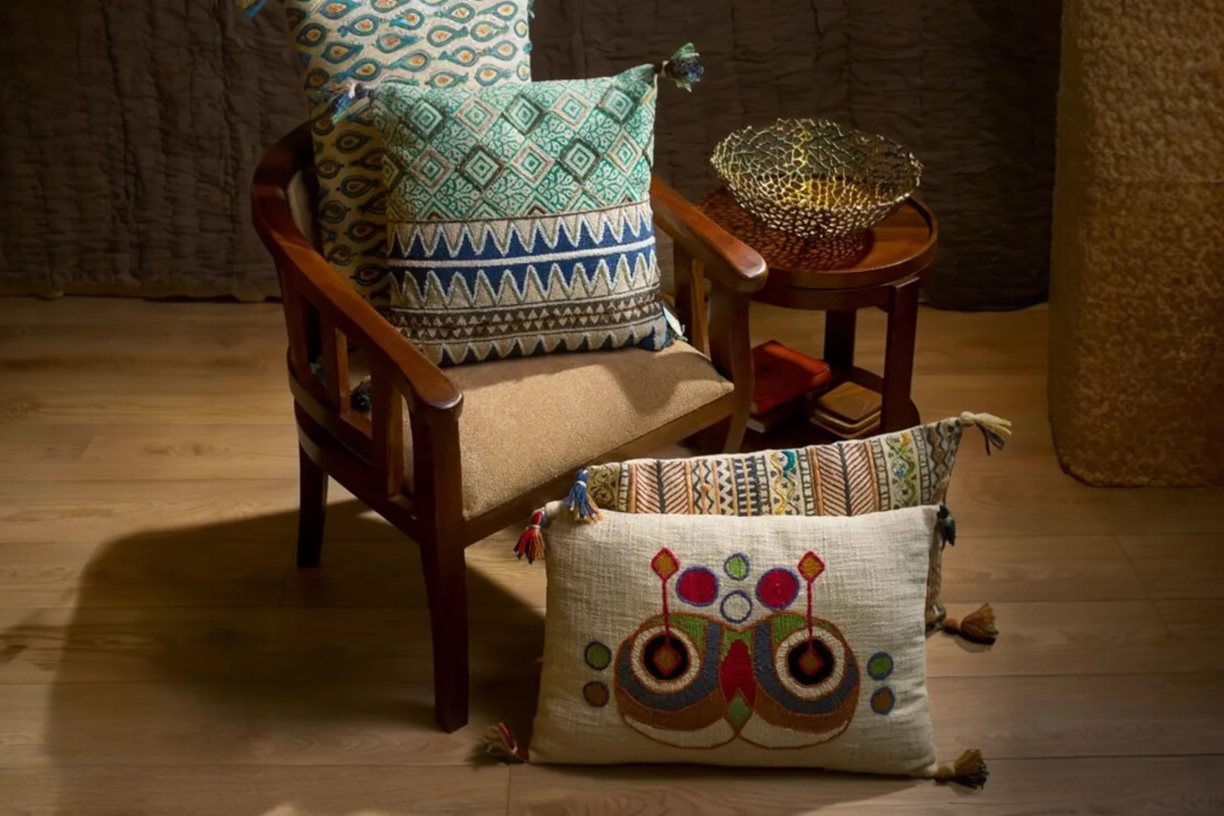 Four different embroidered cushions displayed on a dark wooden chair.