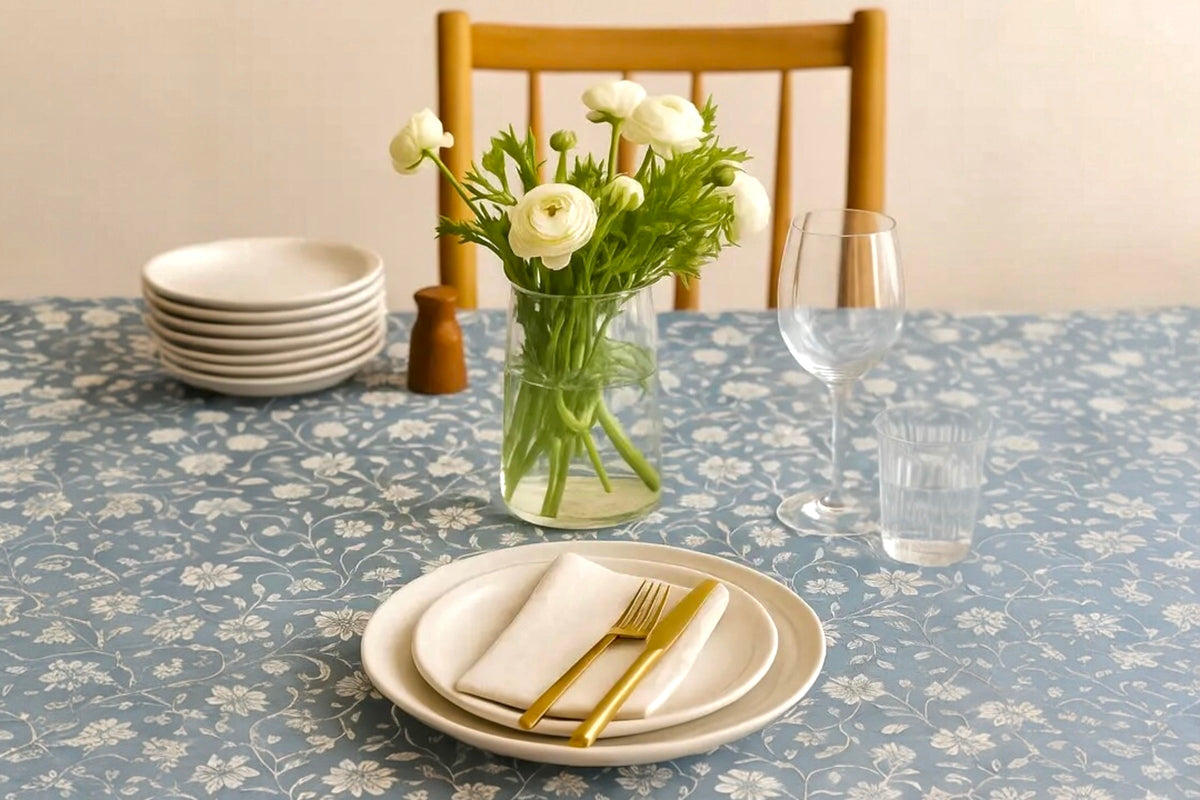 FINCHCRAFT blue cotton table cover with a white floral vine pattern, styled on a dining table with plates and flowers.