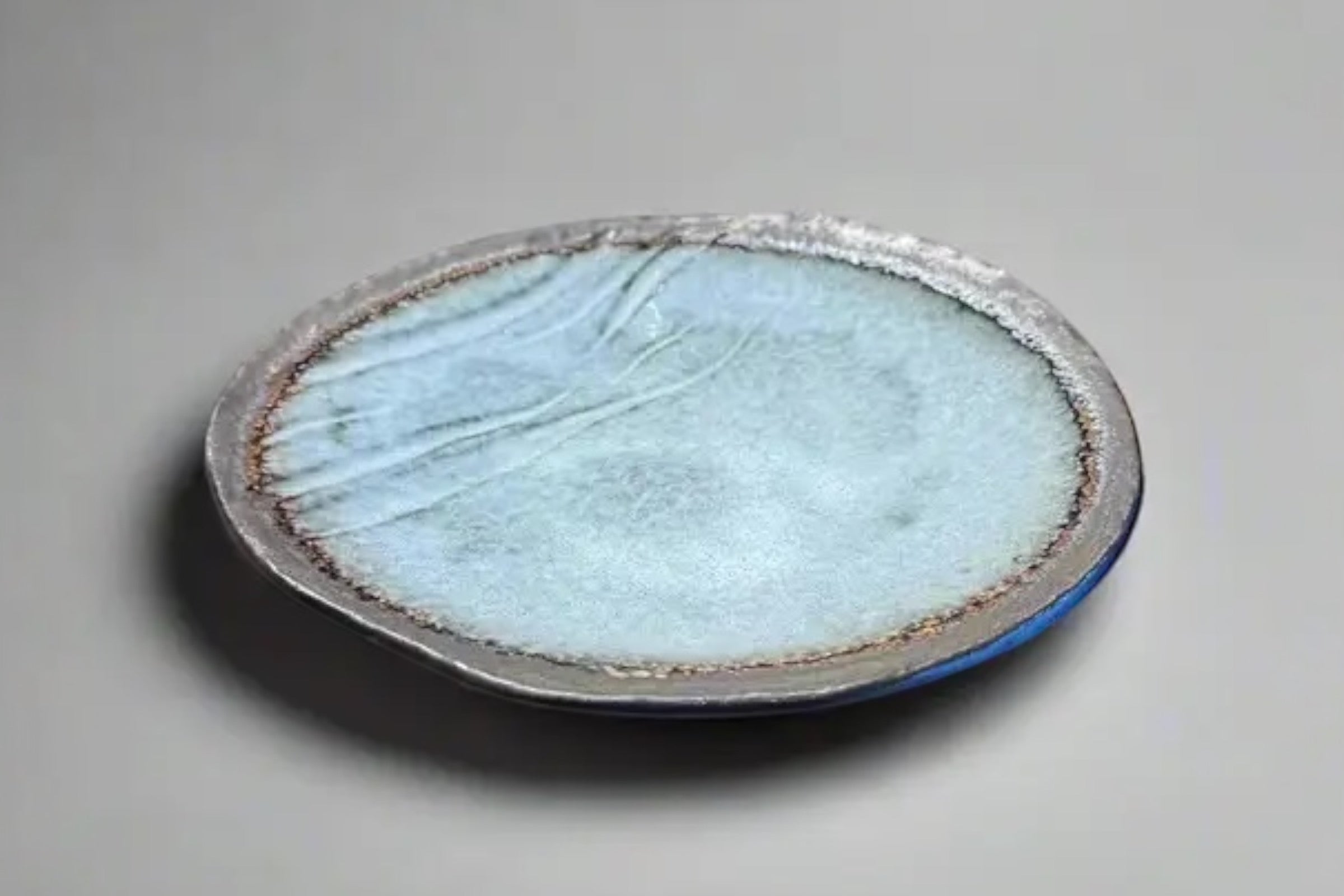 A bisque edged, grey blue Japanese plate on a grey background.