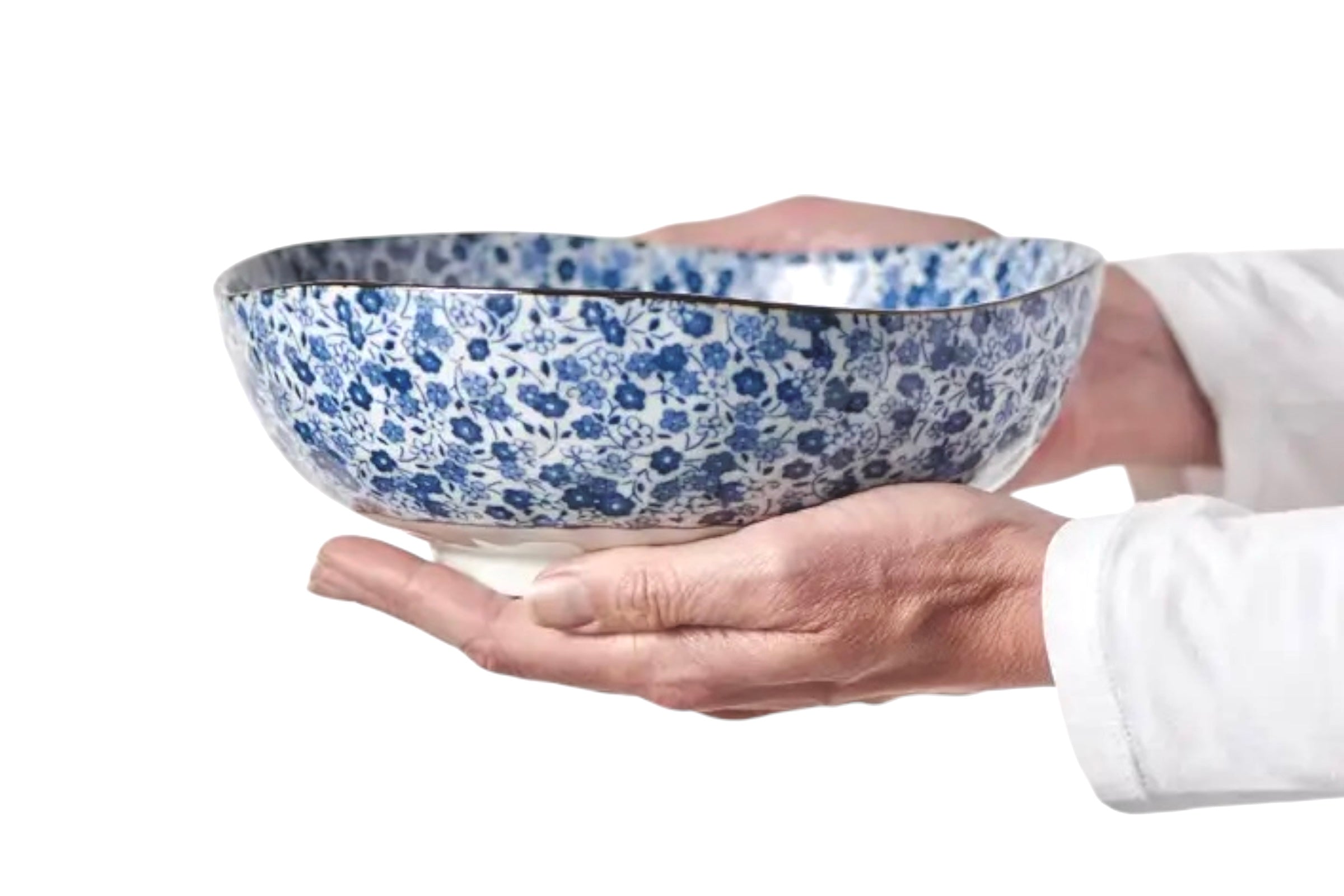 A Japanese rice bowl with a blue daisy design being held in a woman's hands, against a whiote background.
