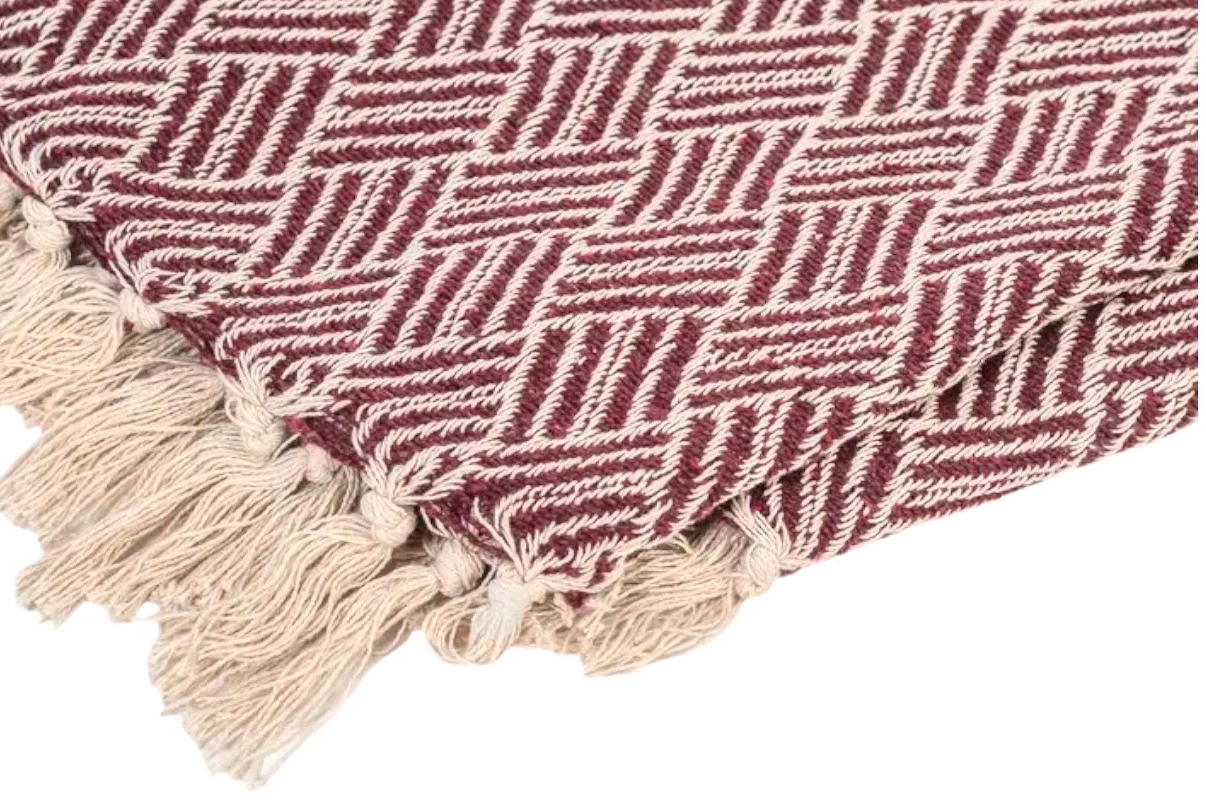 The corner of a burgundy coloured handwoven cotton throw on a white background.