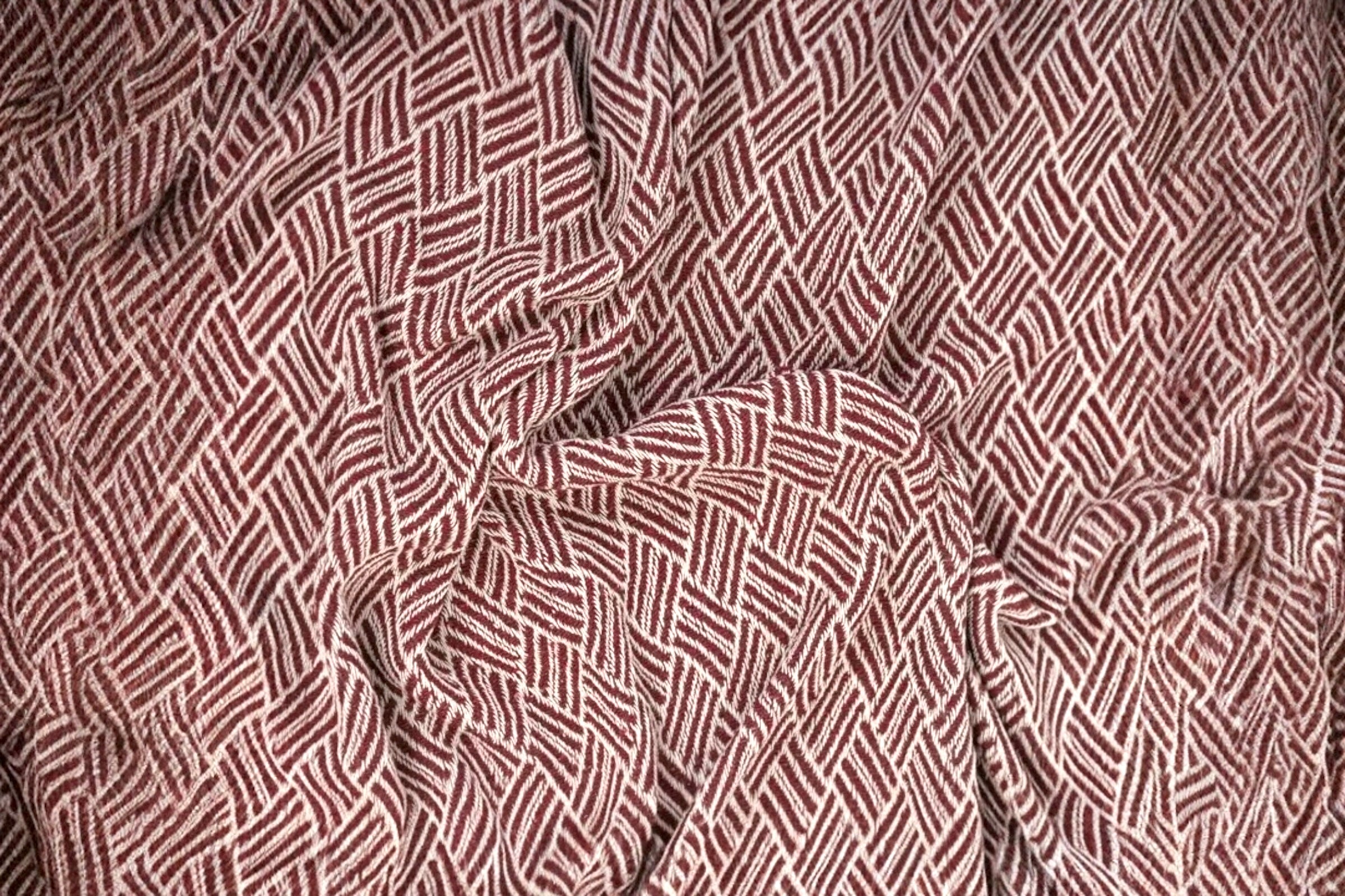 A close up of a burgundy coloured handwoven cotton throw.