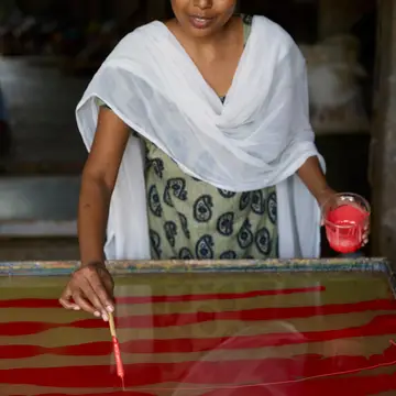 A craftswoman adds marbling detail to  hand made candy stripe design wrapping paper in n indian workshop.