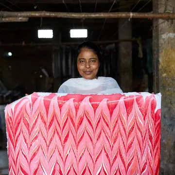 A craftswoman holds up some finished, hand made candy stripe design wrapping paper in n indian workshop.