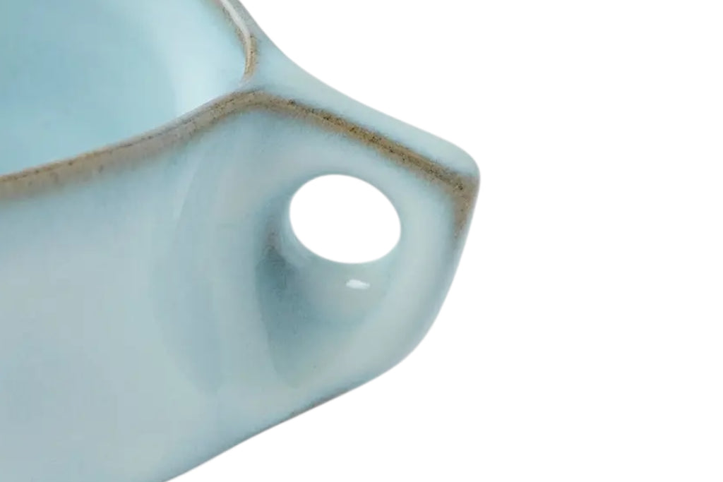 A close up of a ceramic coffee cup with a soft cloud blue glaze and curved handle set against a white background.