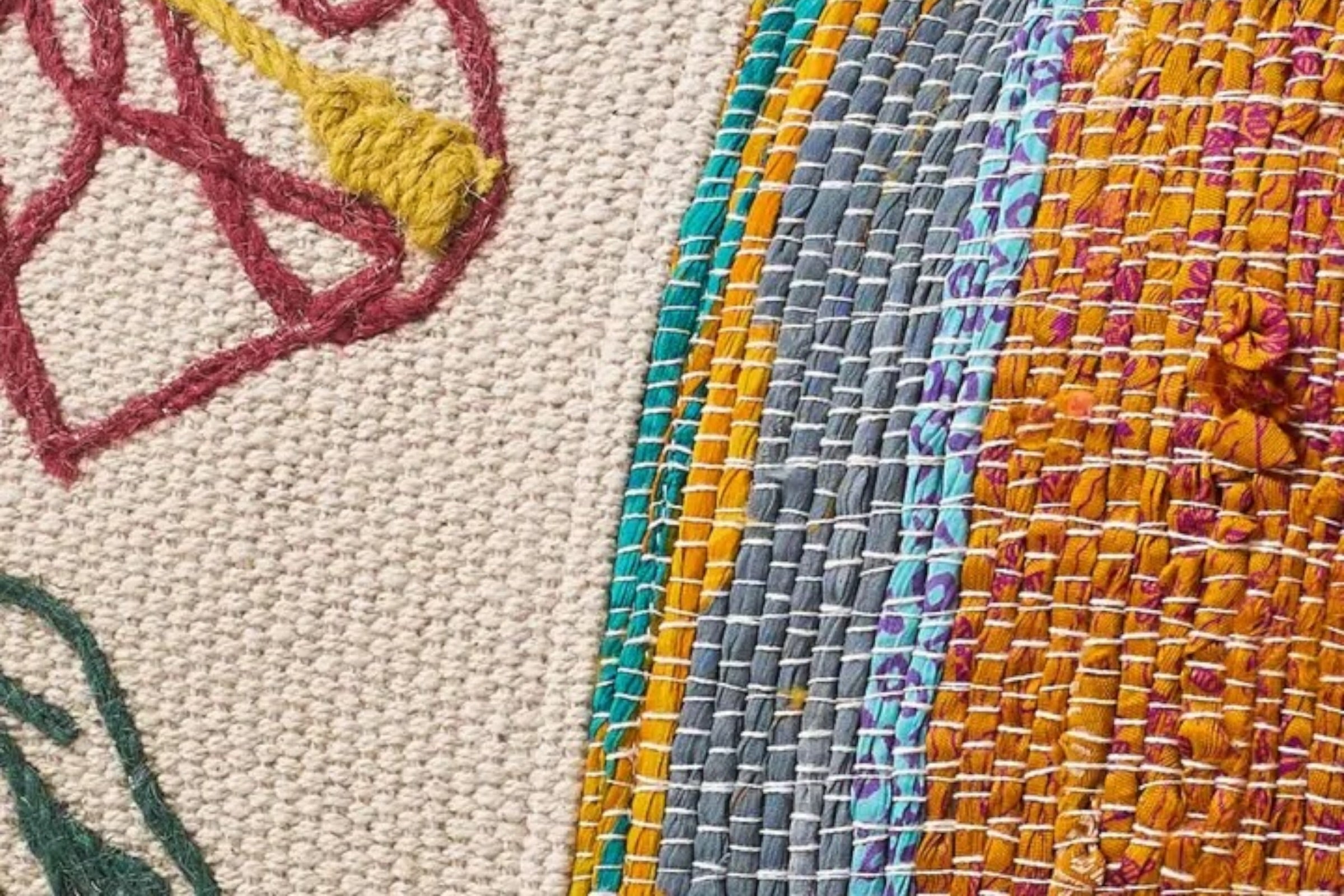 A close up of a red  toned, cotton cushion combining embroidered detail and woven stripes. set against a white background.