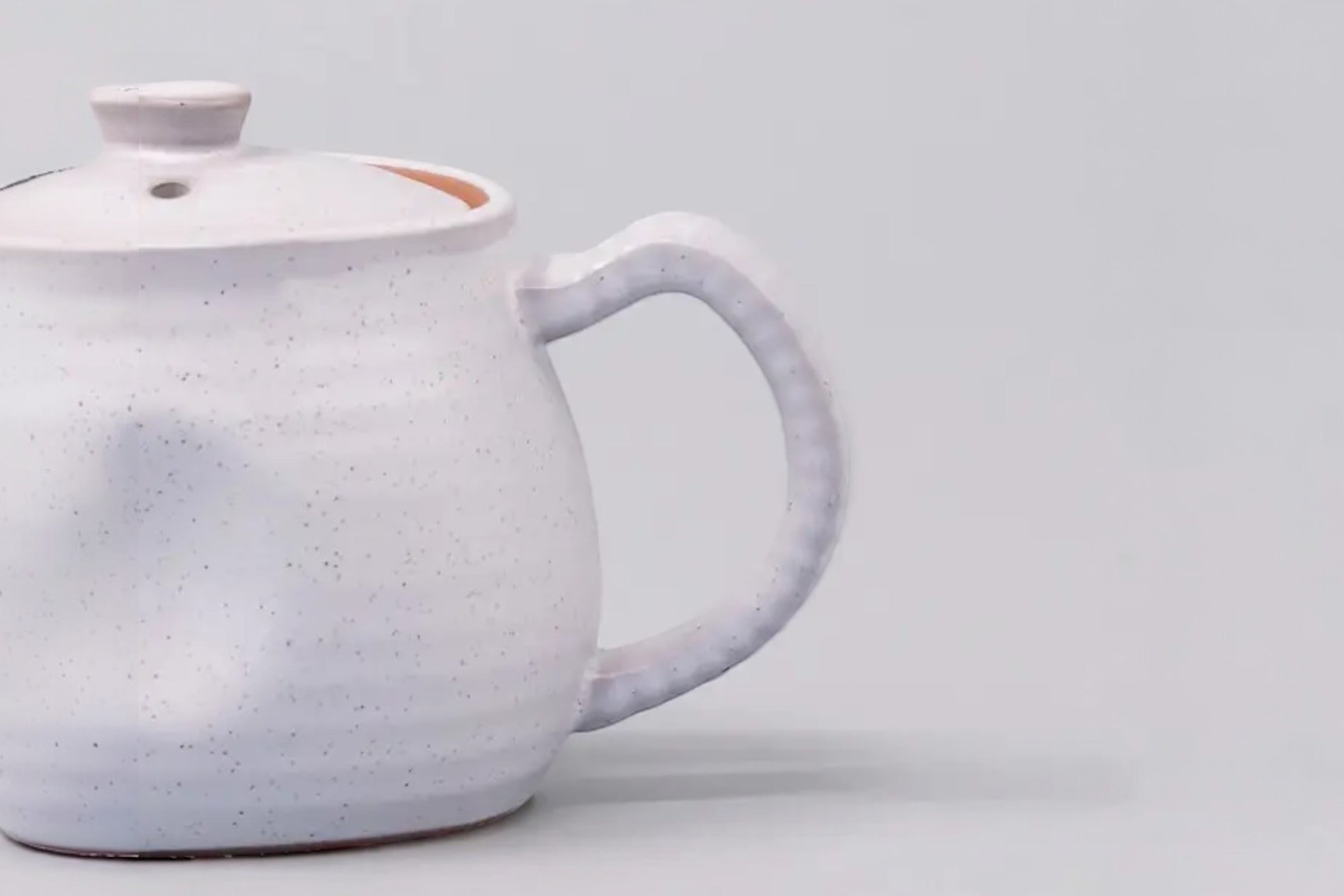 A cut off photo of a white speckled japanese teapot with a ridge design, set against a white background.