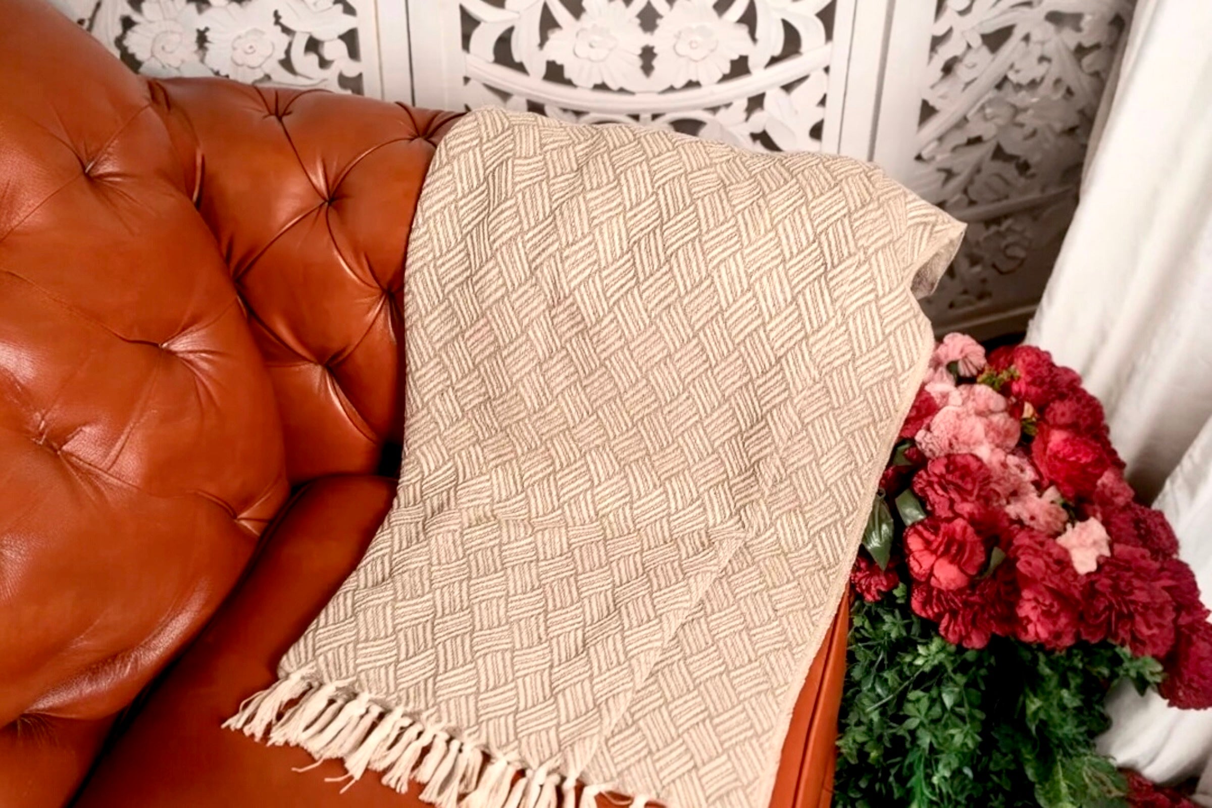 An oatmeal coloured handwoven cotton throw dispayed on a tan leather armchair.