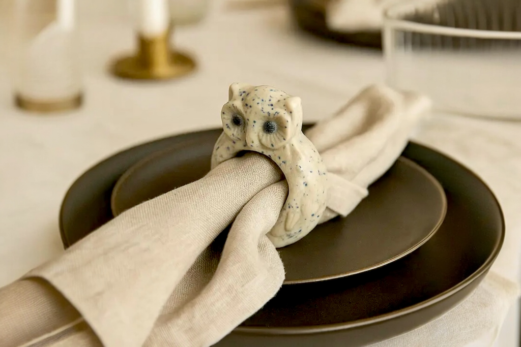An Owl Ceramic Napkin Ring pictures in position with napkin, on a brown table setting.