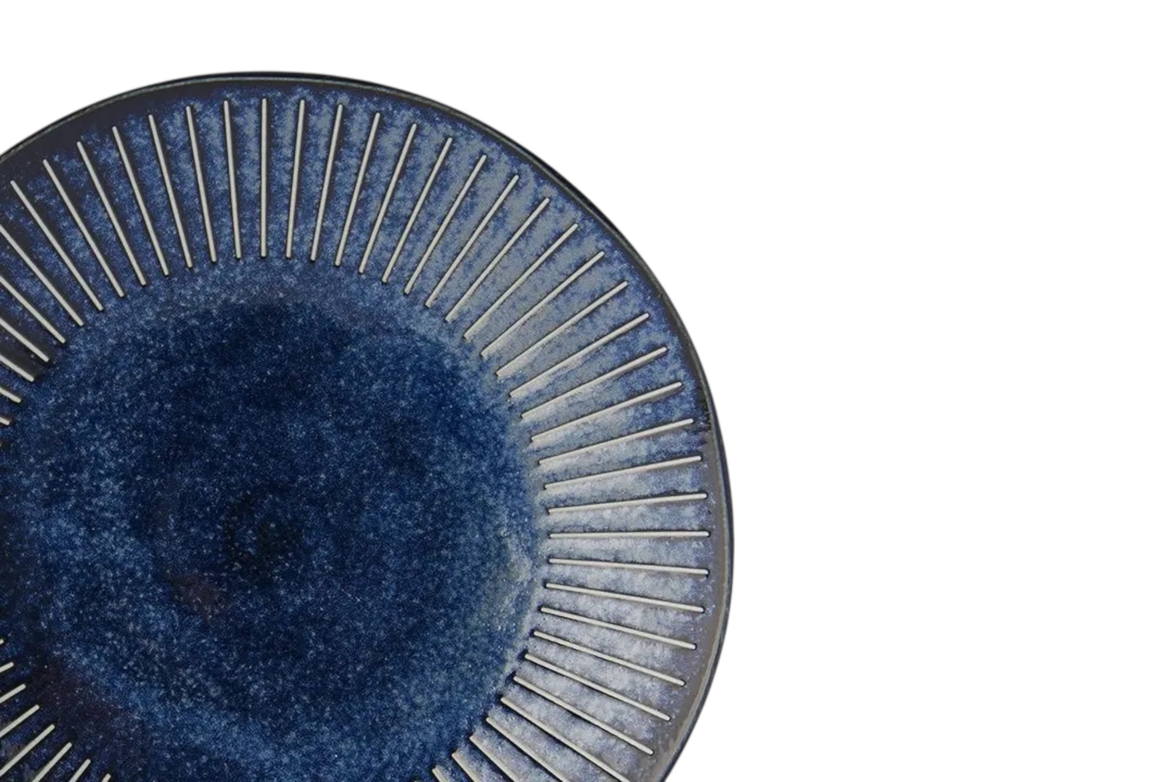 A close up of a porcelain dinner plate with an indigo glaze and fine embossed ridges. Set against a white background.