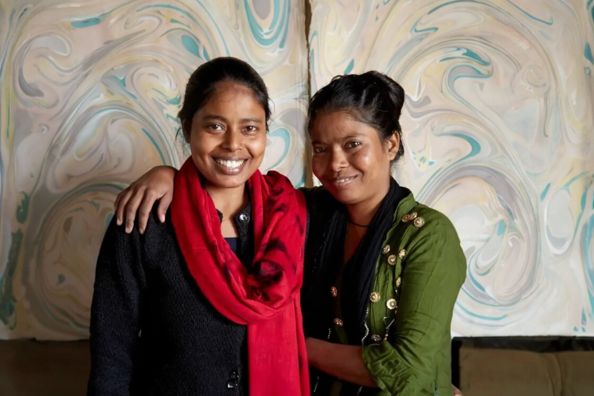 Two craftswomen stand in front of drying, handmade wrapping paper with a rost quartz design.