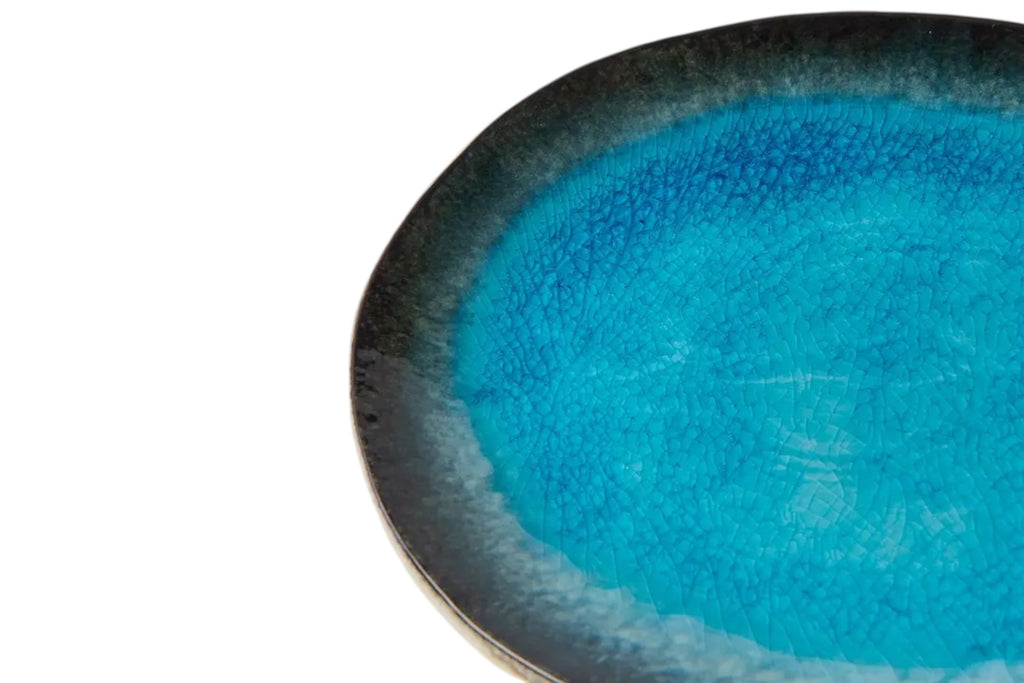A close up of an oval porcelain plate with a soft sky blue glaze and organic outline, set against a white background.