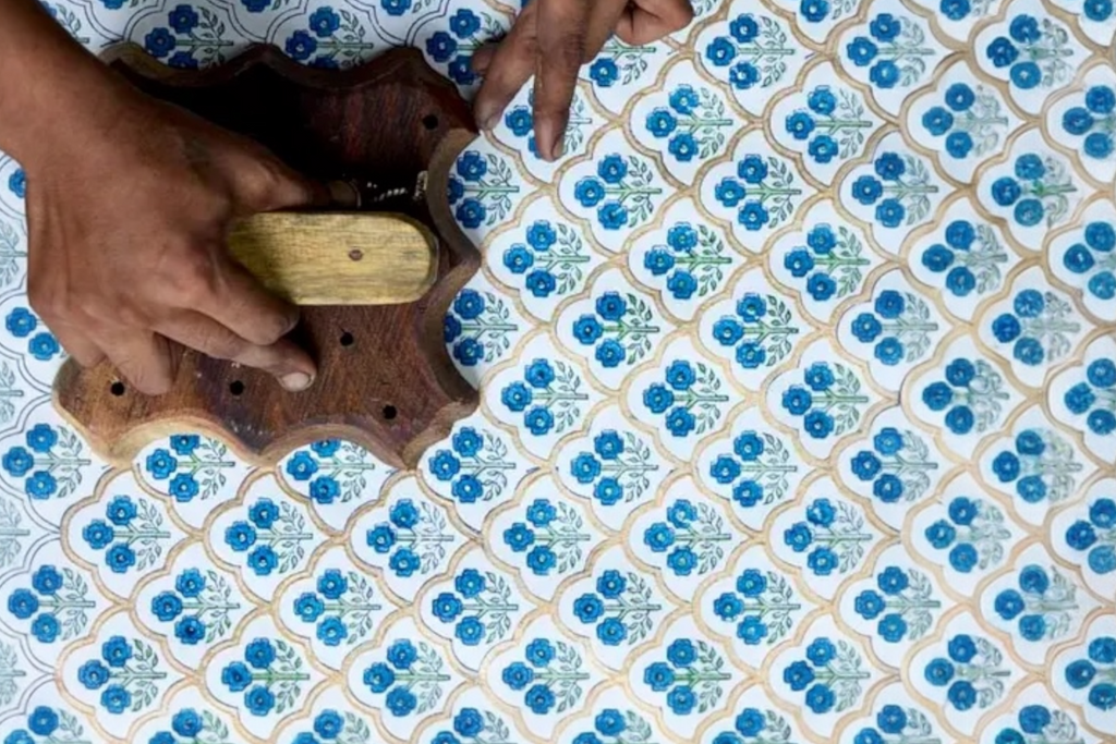 A close up of a craftsman's hands block printing some handmade, trellis indigo design wrapping paper.