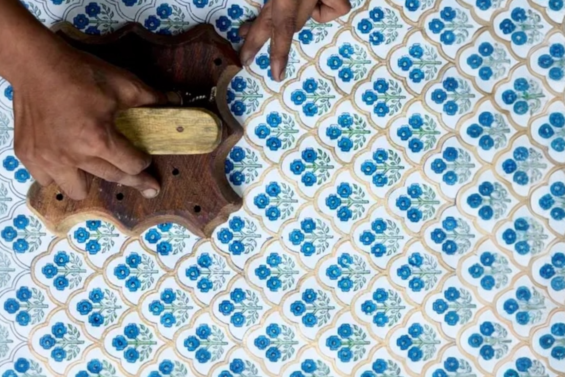 A close up of a craftsman's hands block printing some handmade, trellis indigo design wrapping paper.