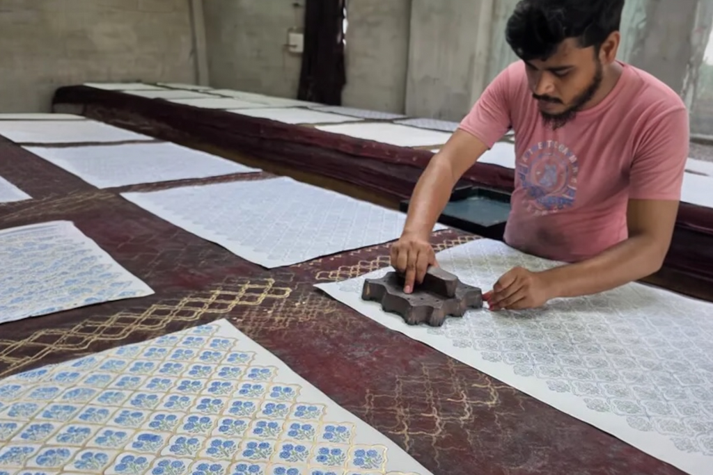 A craftsman works at a long table, block printing handmade, indigo trellis design wrapping paper.